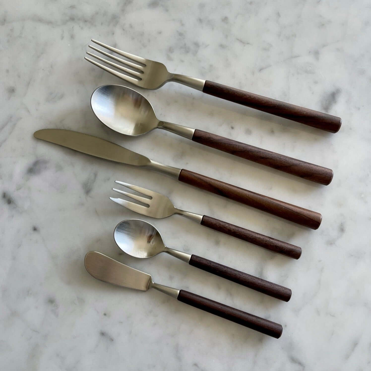 Elegant Rosewood cutlery set with unique natural wood grain handles on a marble surface, featuring forks, spoons, and knives.