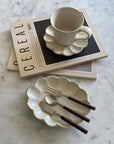 Porcelain flower-shaped Rinka oval plate and cup from Kaneko Kohyo's collection, styled with cutlery on a marble surface.