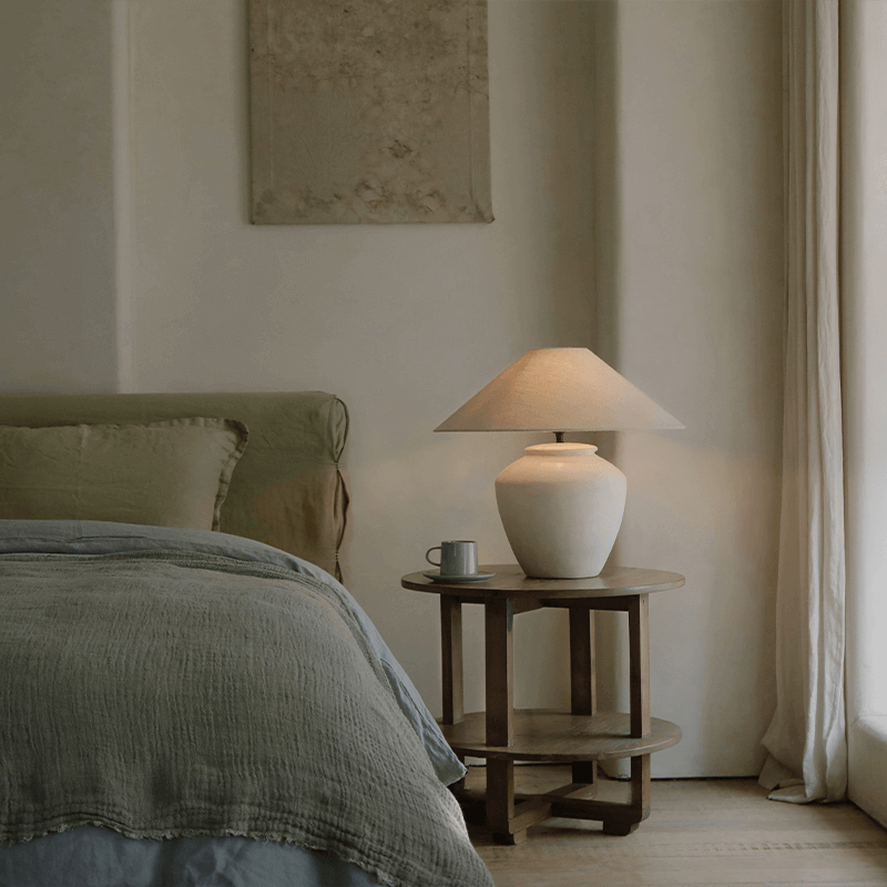 Elegant pot lamp with linen shade on bedside table in cozy bedroom setting.