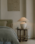 Elegant pot lamp with linen shade on bedside table in cozy bedroom setting.