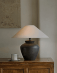 Elegant pottery table lamp with linen shade on wooden furniture, enhancing decor with adjustable warm lighting.