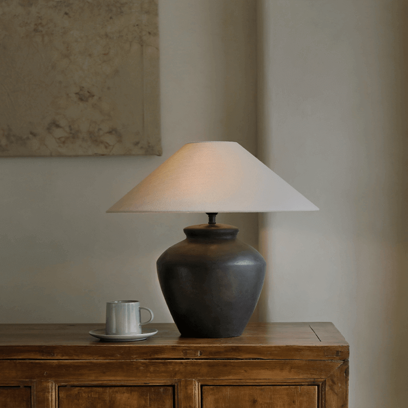 Elegant pottery table lamp with linen shade on wooden furniture, enhancing decor with adjustable warm lighting.