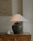 Elegant pottery table lamp with linen shade on wooden furniture, enhancing decor with adjustable warm lighting.