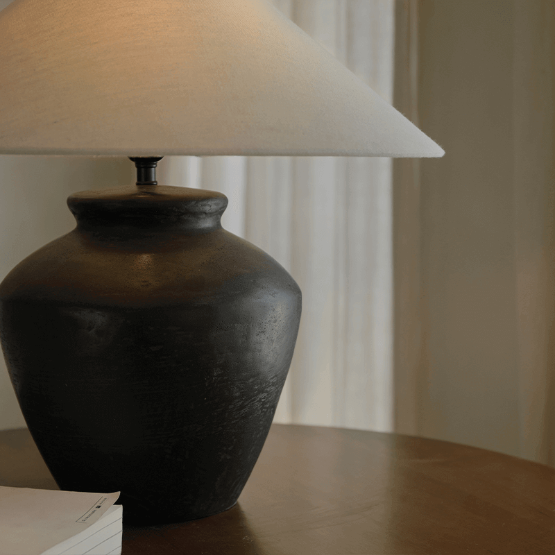 Elegant clay pot lamp with a linen shade on a wooden table, perfect for creating a quiet and comfortable space environment.