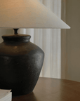 Elegant clay pot lamp with a linen shade on a wooden table, perfect for creating a quiet and comfortable space environment.
