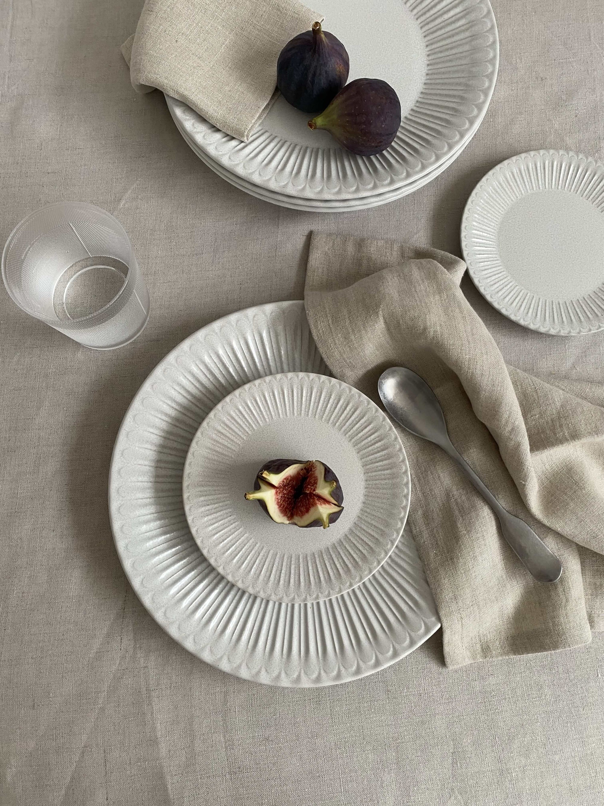 Elegant white porcelain plates with soft lace edges and figs on a neutral tablecloth, evoking nostalgia and sophistication.