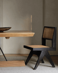 Wood-mounted dining chair with rattan weaving, handcrafted from imported teak, displayed alongside a wooden table in a cozy setting.