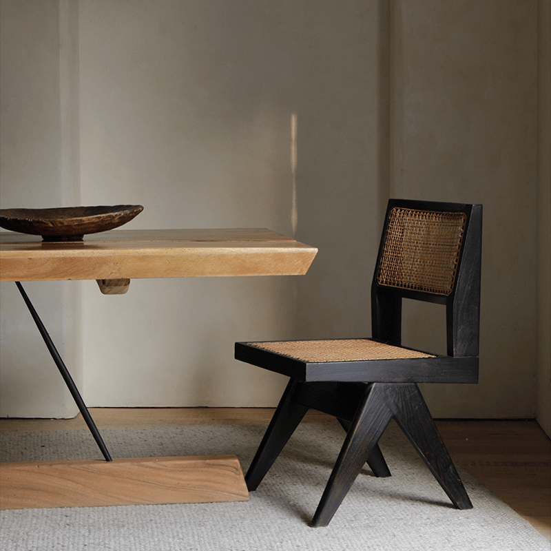 Wood-mounted dining chair with rattan weaving, handcrafted from imported teak, displayed alongside a wooden table in a cozy setting.