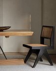Wood-mounted dining chair with rattan weaving, handcrafted from imported teak, displayed alongside a wooden table in a cozy setting.
