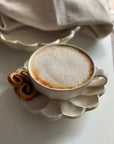 Rinka porcelain soup cup with latte foam on floral plate set alongside spiral pastries