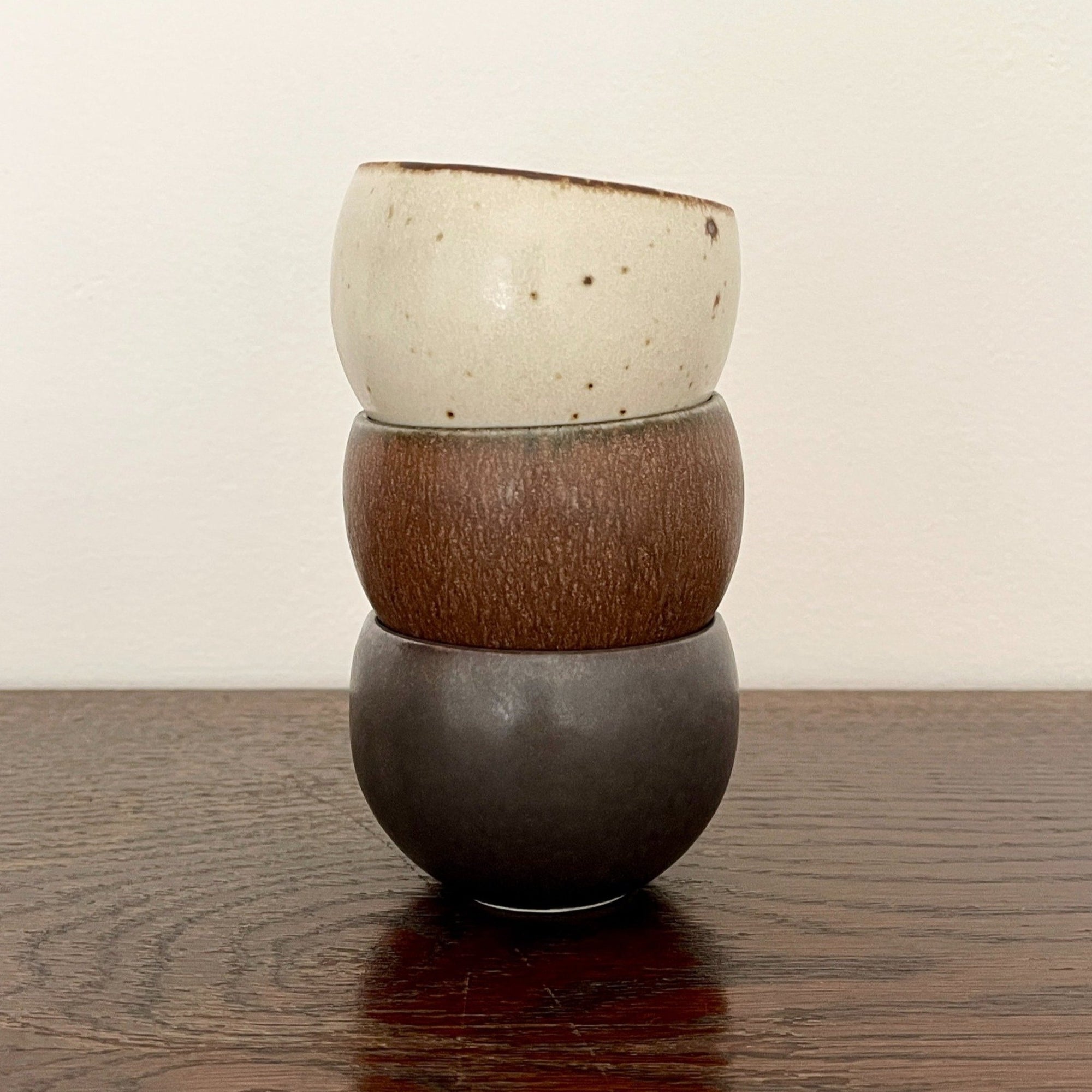 Stack of three Rila Tea Cups with textured surfaces in warm matte colors on a wooden table.