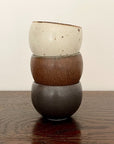 Stack of three Rila Tea Cups with textured surfaces in warm matte colors on a wooden table.
