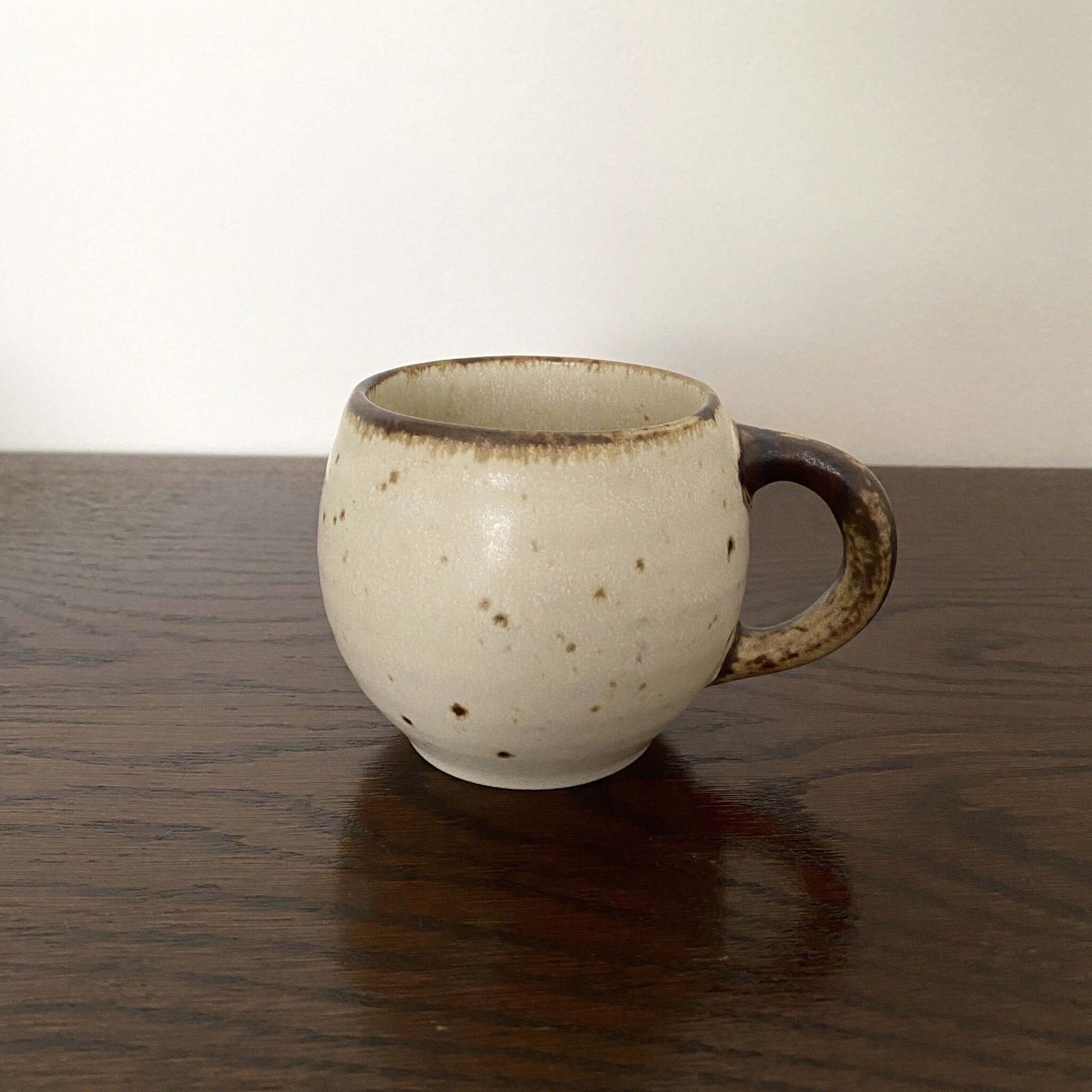 Ivory mug with a rustic handle, crafted from textured porcelain by Kaneko Kohyo, sitting on a wooden table.