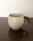 Ivory mug with a rustic handle, crafted from textured porcelain by Kaneko Kohyo, sitting on a wooden table.