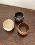 Three stackable Rila Tea Cups by Kaneko Kohyo, textured and matte colored, perfect for tea or desserts, displayed on a wooden surface.