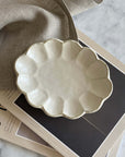 Porcelain Rinka Oval Plate with flower shape from Kaneko Kohyo, set on a stack of magazines, showcasing its delicate craftsmanship.