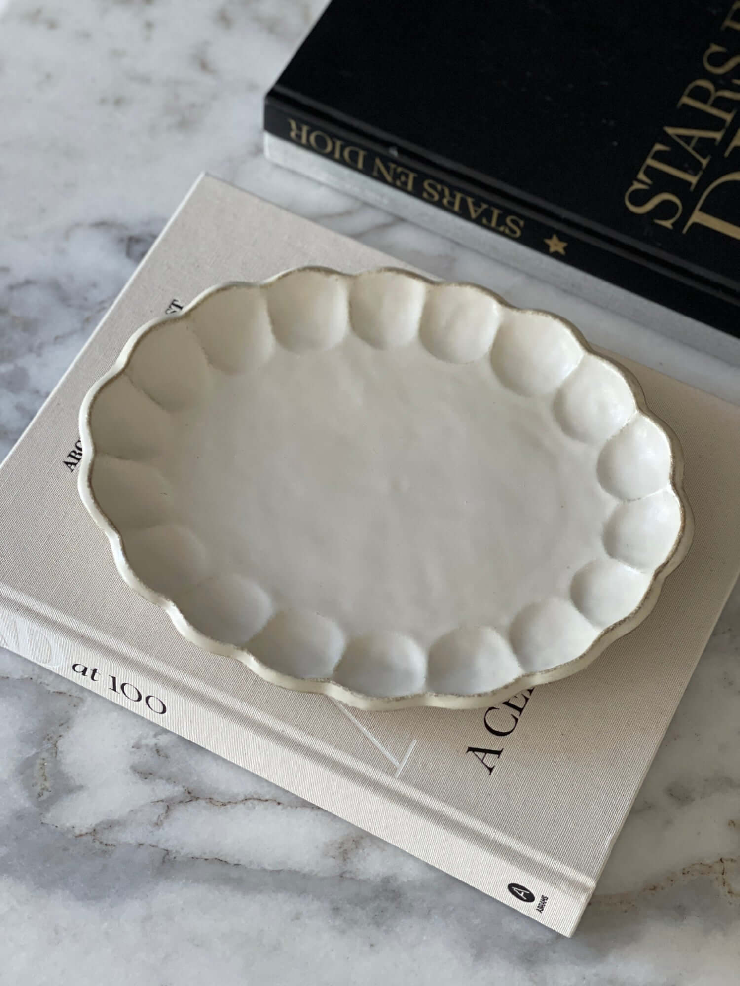 Rinka Oval Plate made of delicate porcelain with a flower shape, resting on books, part of the Kaneko Kohyo Rinka Collection.