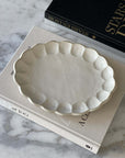 Rinka Oval Plate made of delicate porcelain with a flower shape, resting on books, part of the Kaneko Kohyo Rinka Collection.