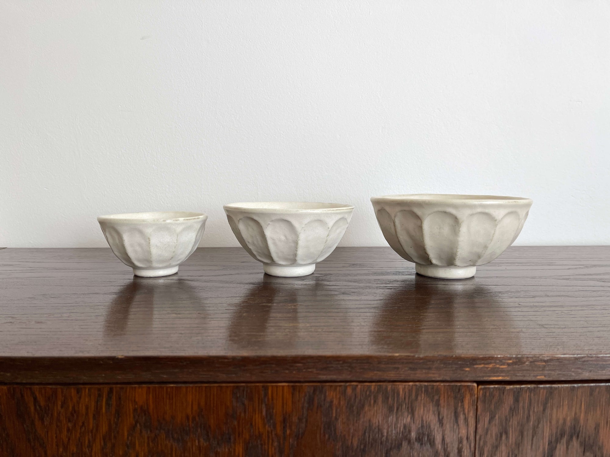 Three handmade white Rinka soup bowls with scalloped design, displayed on a wooden surface. Different sizes, perfect for modern dining.