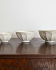 Three handmade white Rinka soup bowls with scalloped design, displayed on a wooden surface. Different sizes, perfect for modern dining.