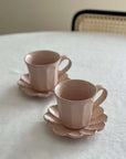 Pink porcelain Rinka Mug & Plate Set on a table, showcasing handmade design with scalloped edges, made in Japan.
