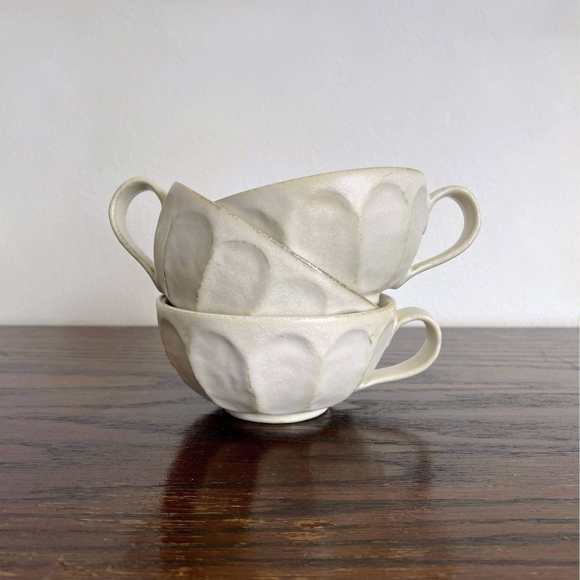 Stack of handcrafted porcelain Rinka soup cups with delicate flower design by Kaneko Kohyo on a wooden table.
