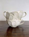 Stack of handcrafted porcelain Rinka soup cups with delicate flower design by Kaneko Kohyo on a wooden table.