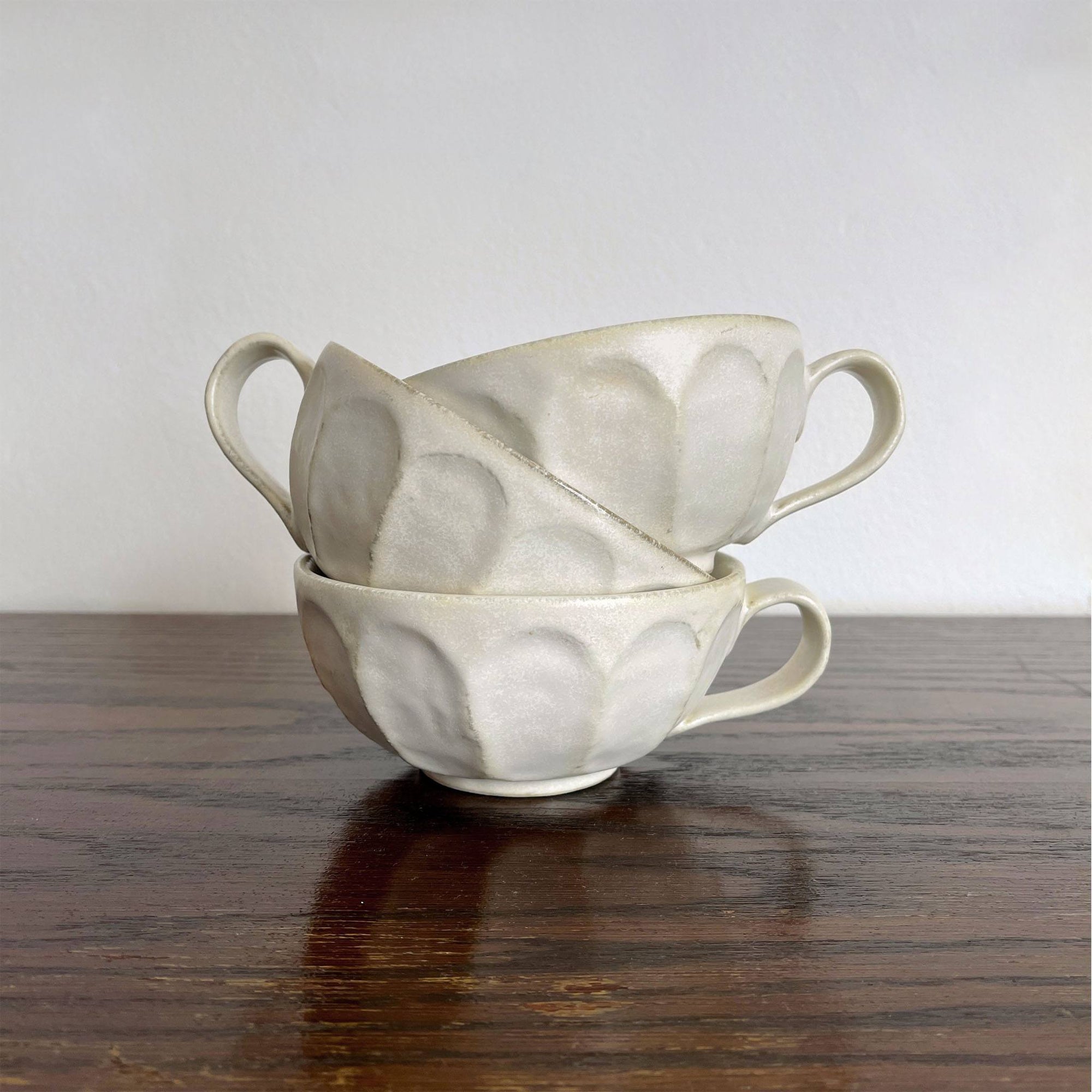 Stack of Kaneko Kohyo's handcrafted Rinka porcelain soup cups with flower shape on wooden table, perfect for enhancing table setting.