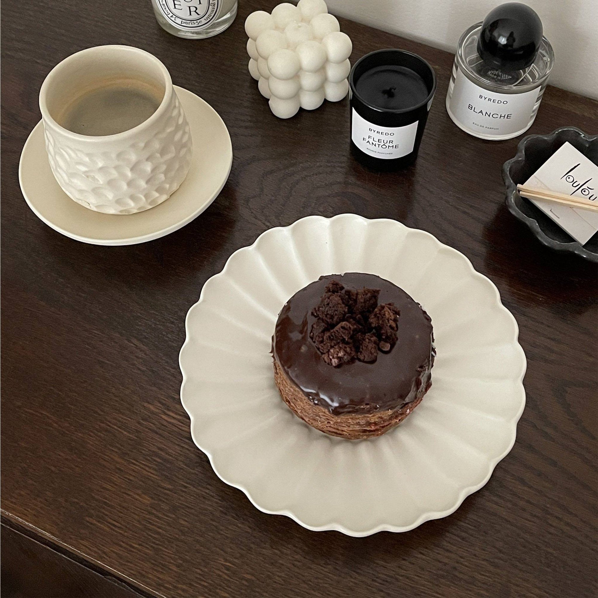 Elegant white Rinka Plate by Yoshida Pottery holding a chocolate dessert, styled with candles and a textured mug on a wooden table.