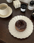 Elegant white Rinka Plate by Yoshida Pottery holding a chocolate dessert, styled with candles and a textured mug on a wooden table.
