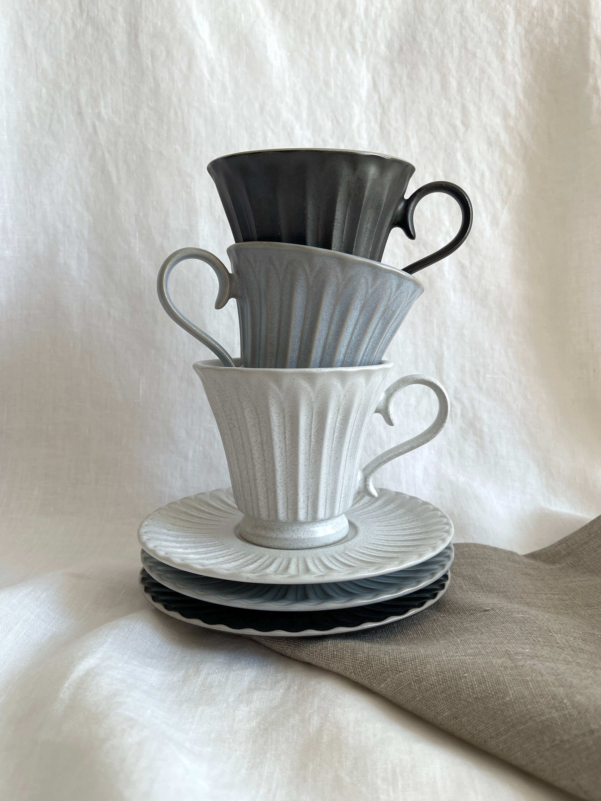 Elegant Storia tall coffee cups stacked on saucers, featuring a soft flecked finish that reflects nostalgia and sophistication.
