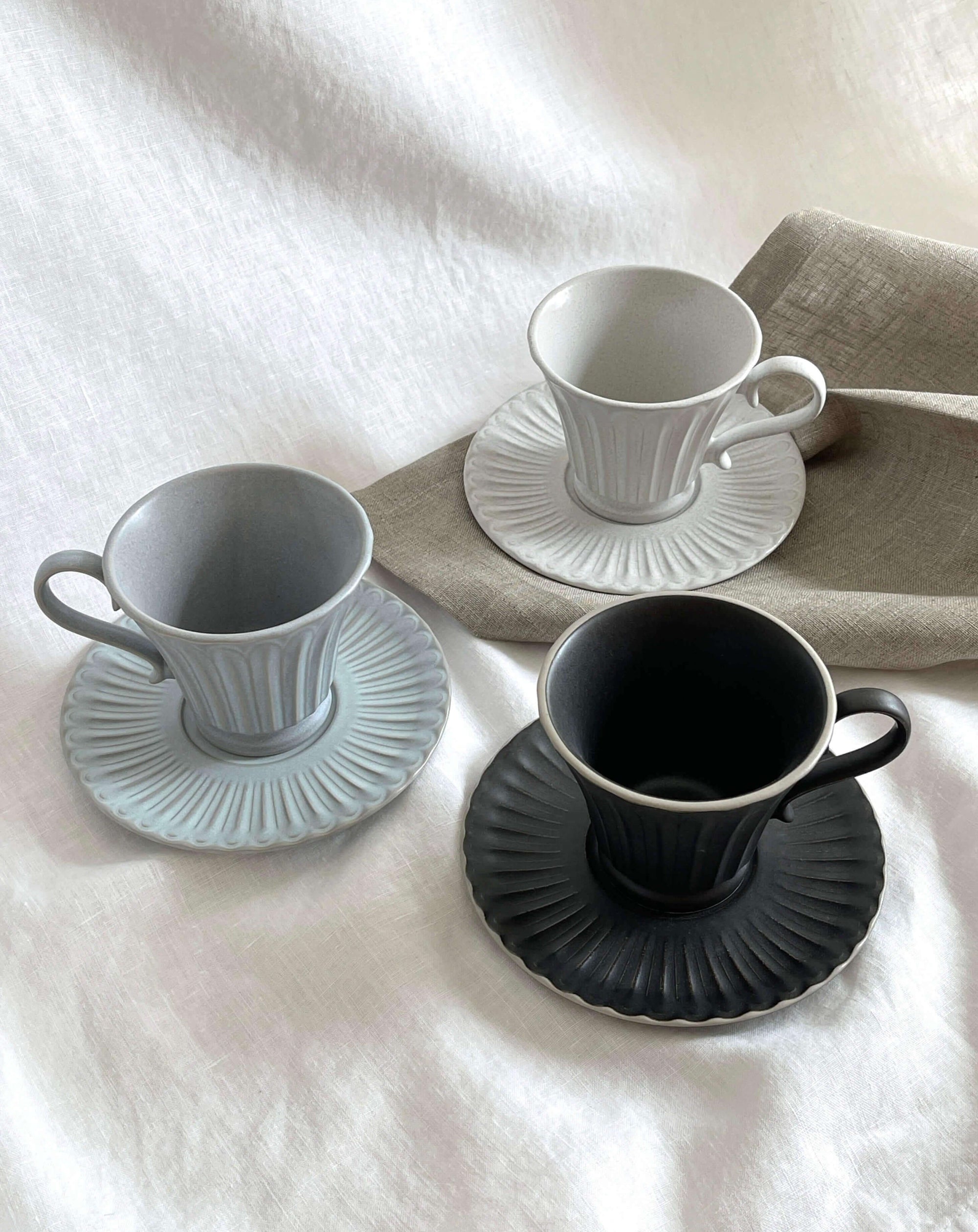 Elegant Storia Tall Coffee Cup & Saucer set in three colors, featuring a high-quality earthenware texture and antique-style design.