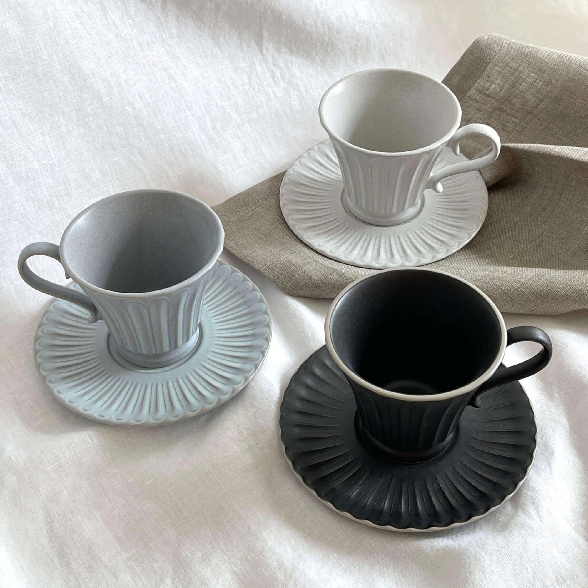 Storia Tall Coffee Cup & Saucer set in porcelain, showcasing elegant flecked lacquer finish in three colors on a soft table setting.