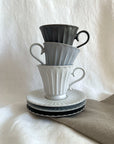 Elegant Storia tall coffee cups stacked on saucers, featuring a soft flecked finish that reflects nostalgia and sophistication.