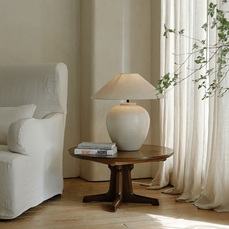Egg Shaped Clay Pot Table Lamp on wooden table with soft linen shade, next to white sofa creating a peaceful room ambiance