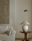 Egg-shaped clay pot table lamp on wooden table beside beige sofa in serene living room setting with minimalist decor.