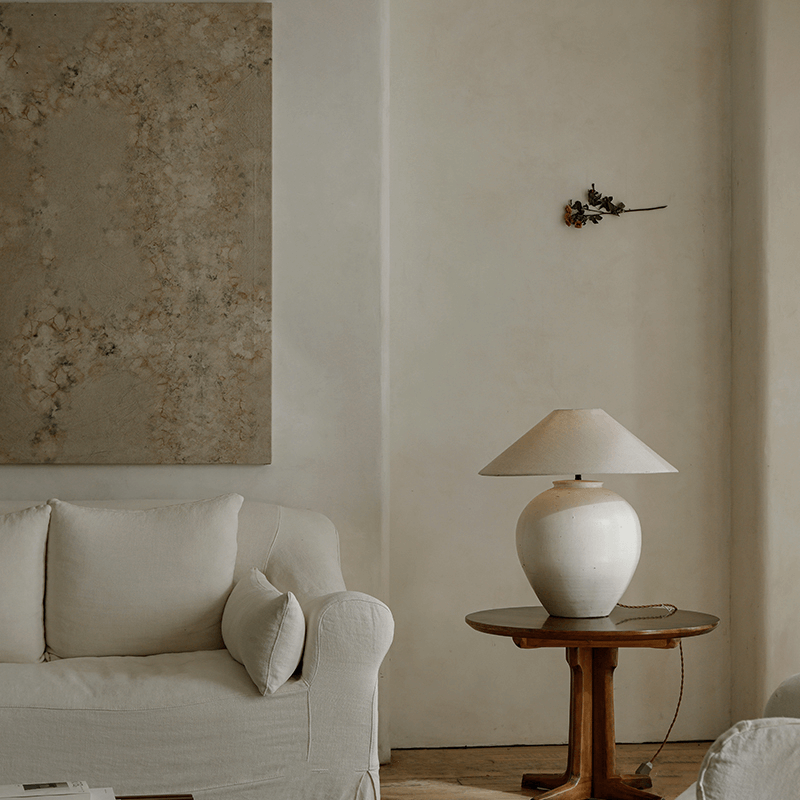 Egg-shaped clay pot table lamp on wooden table beside beige sofa in serene living room setting with minimalist decor.