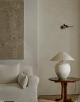Egg-shaped clay pot table lamp on wooden table beside beige sofa in serene living room setting with minimalist decor.