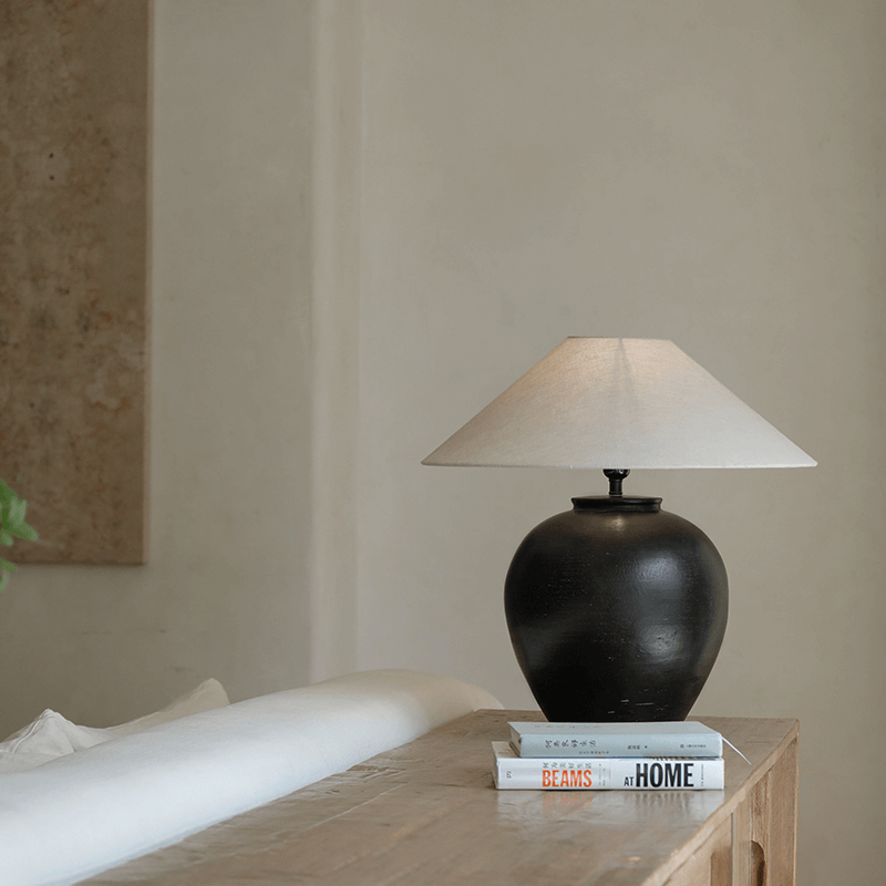 Egg-shaped clay pot table lamp with linen shade on a wooden table setting a peaceful ambiance in a cozy room.
