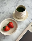 Ceramic cup with green tea, white plate with strawberries, and magazine on marble table.
