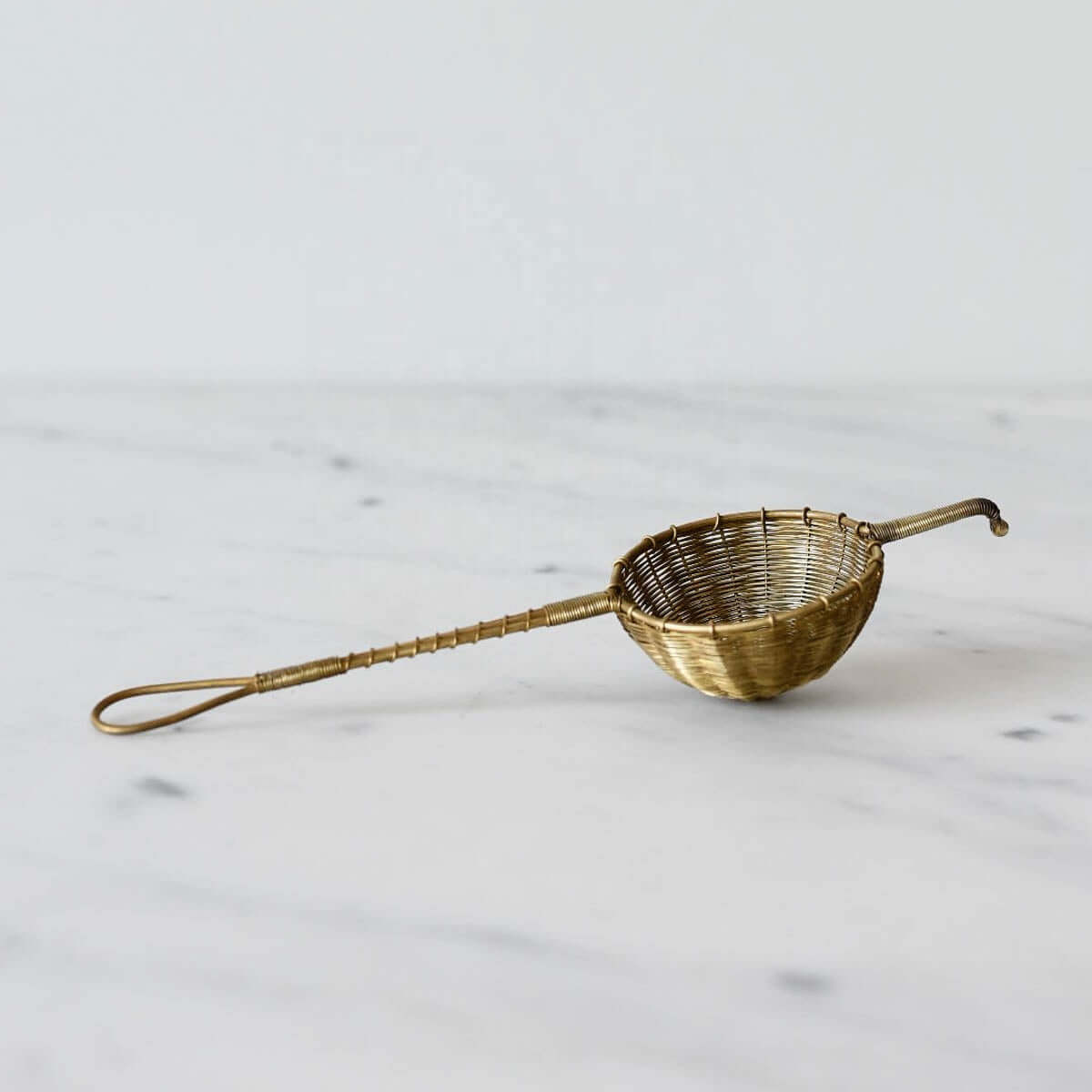 Handwoven brass tea filter for loose leaf tea on a marble surface.