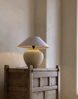 Wabi-Sabi handmade table lamp with milky white and black pottery body, linen lampshade on rustic wooden table in peaceful setting.