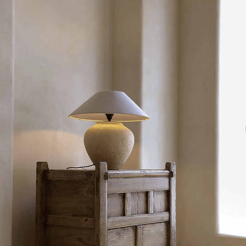 Wabi-Sabi handmade table lamp with milky white and black pottery body, linen lampshade on rustic wooden table in peaceful setting.