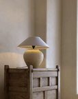 Wabi-Sabi handmade table lamp with milky white and black pottery body, linen lampshade on rustic wooden table in peaceful setting.