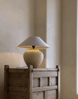 Wabi-Sabi handmade table lamp with milky white and black pottery body, linen lampshade on rustic wooden table in peaceful setting.
