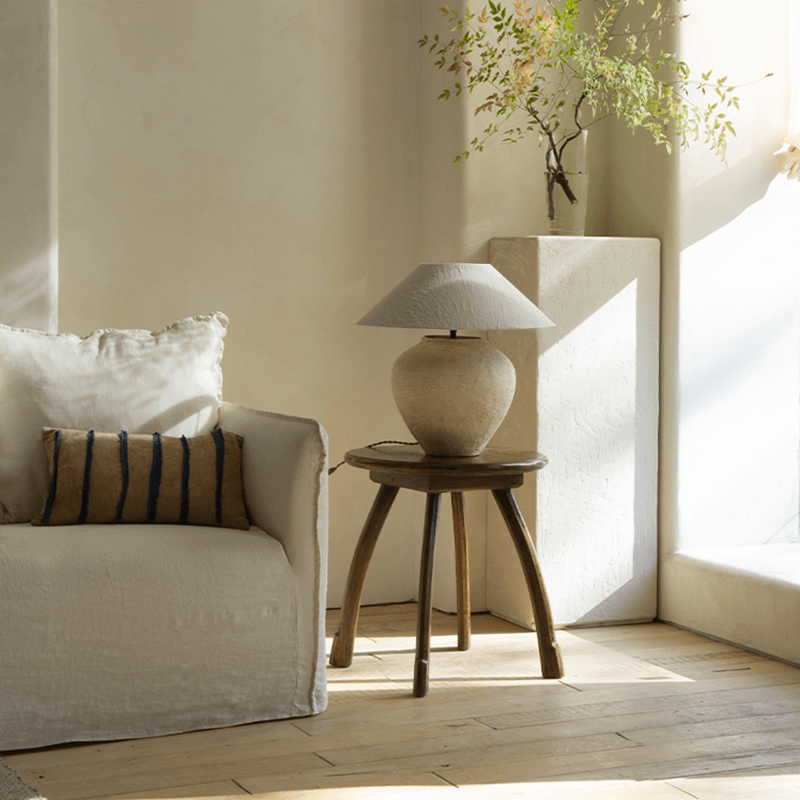 Wabi-Sabi style handmade table lamp with linen shade on wooden stand in a peaceful living room setting.