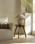 Wabi-Sabi style handmade table lamp with linen shade on wooden stand in a peaceful living room setting.