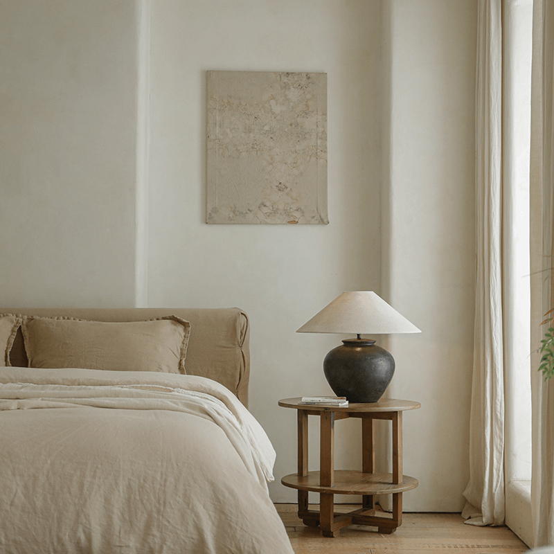 Wabi-sabi style handmade table lamp with pottery body and linen shade in a minimalist bedroom setting