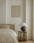 Wabi-sabi style handmade table lamp with pottery body and linen shade in a minimalist bedroom setting