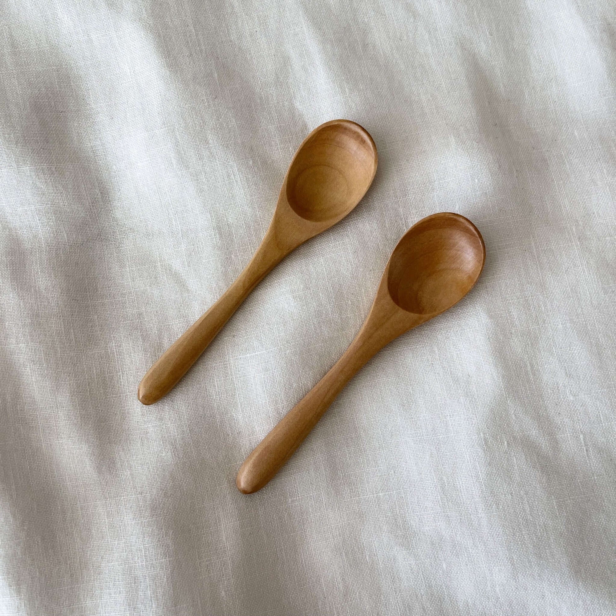 Two wooden teaspoons on a white cloth, perfect for tea or coffee, made from natural wood, 12.1cm in length.